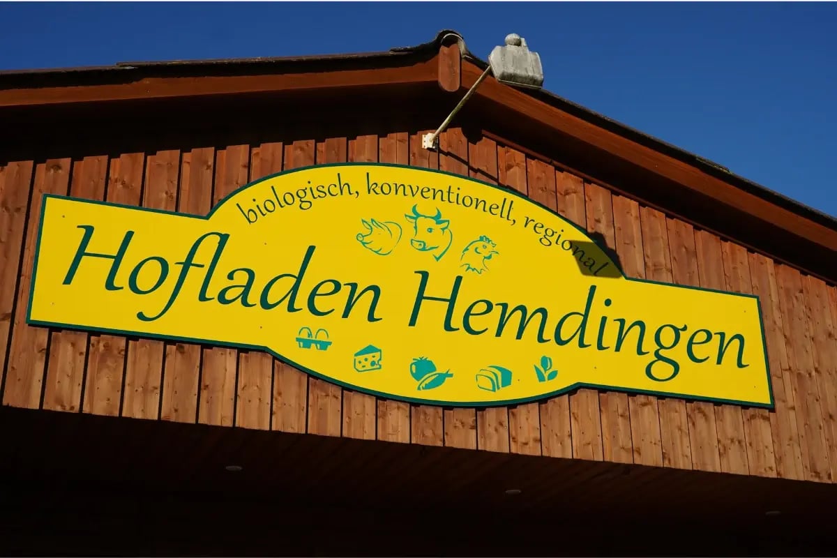 Gelbes Schild des Hofladens Hemdingen an der Holzfassade.