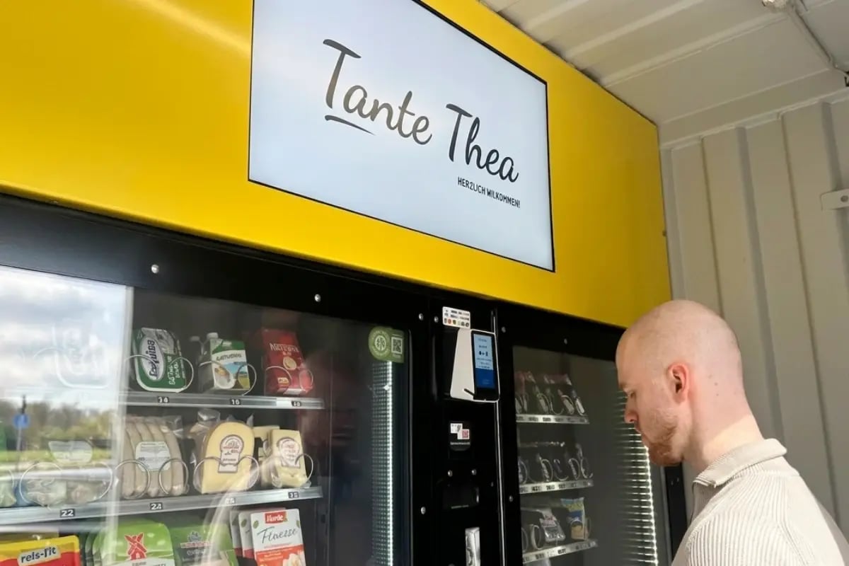 Kunde vor einem Tante-Thea-Automaten mit digitalem Werbebildschirm.